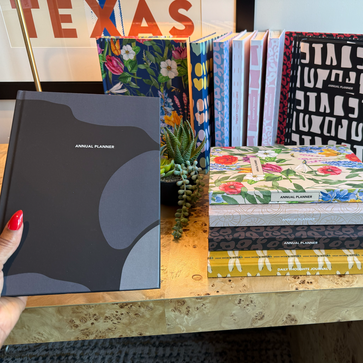 Collection of planners and journals on a surface with a hand holding a black planner.