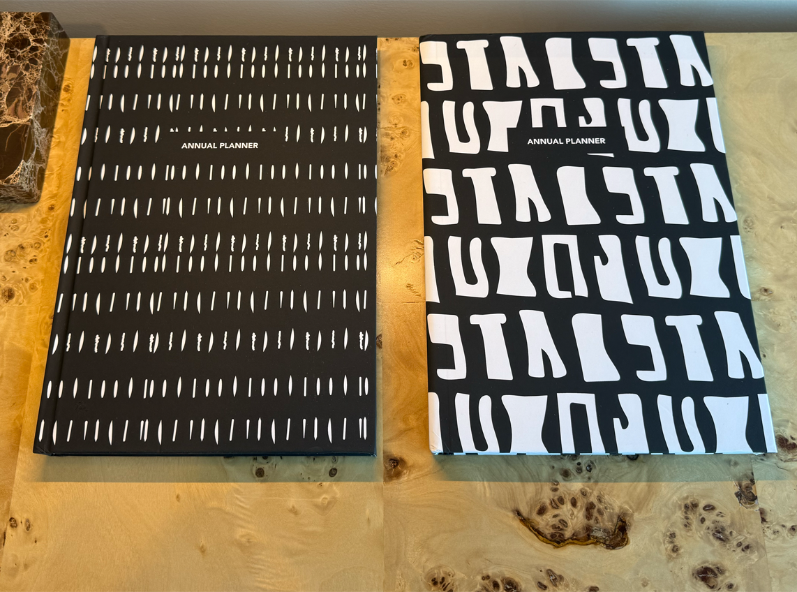 Two black planners with white batik patterns on a desk
