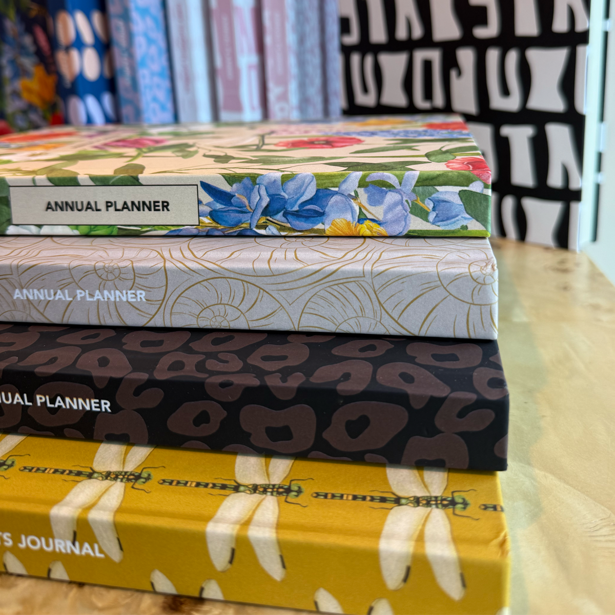 Stack of planners with floral, geometric, and animal print covers on a wooden surface.