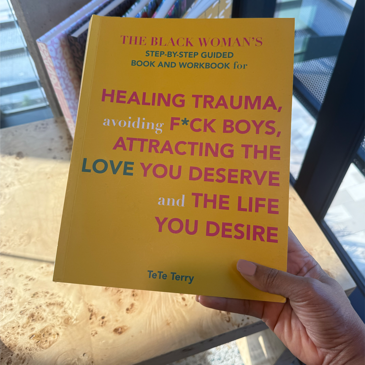 Book titled 'The Black Woman's Step-by-Step Guided Book and Workbook' held by a hand on a des.