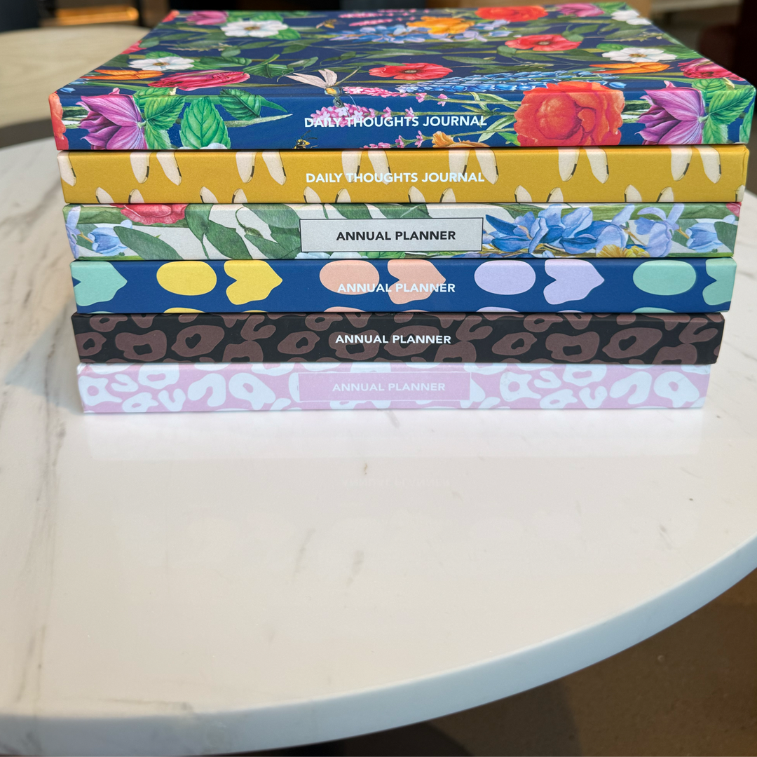 Stack of colorful planners and journals on a white marble table