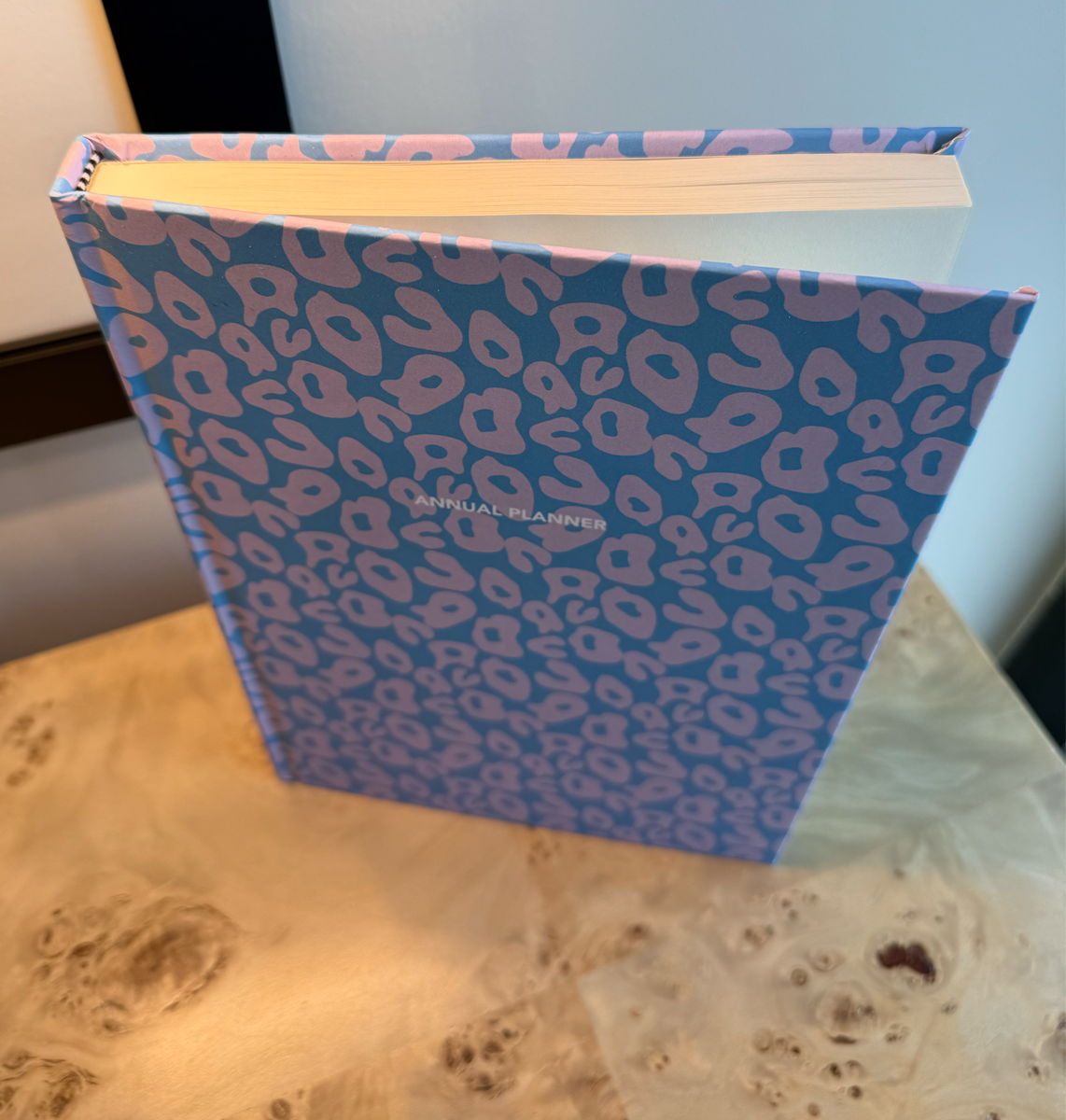 Blue planner with pink leopard print on a wooden surface