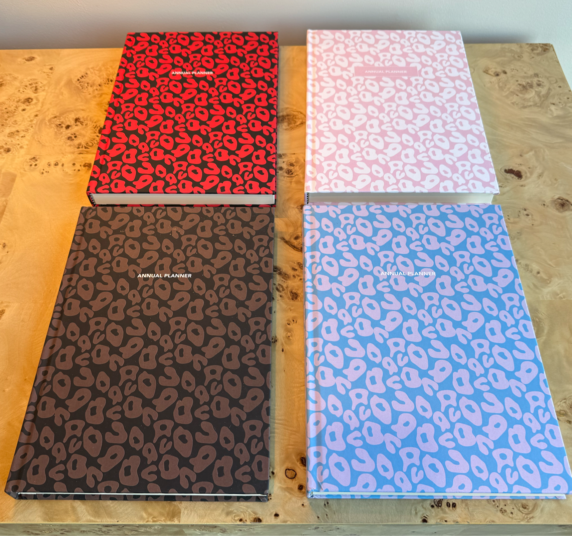 Four planners with leopard print patterns on a wooden surface