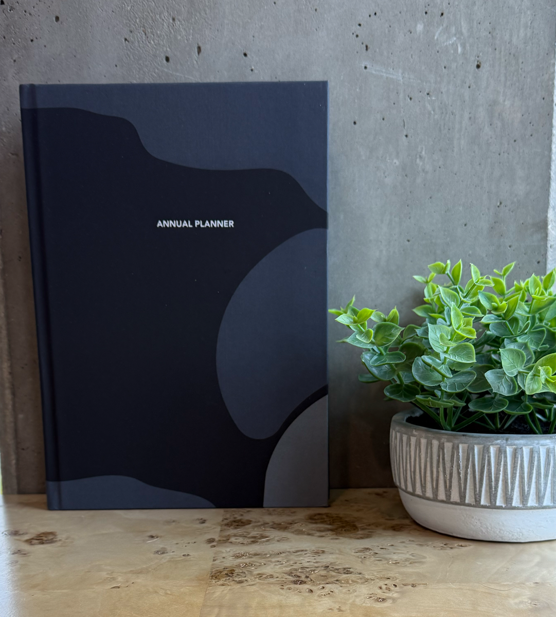 Black annual planner on a wooden desk with a potted plant in the background