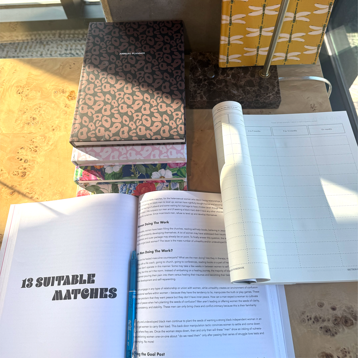 Open book with text on a desk next to closed notebooks by Feminine Pedestal