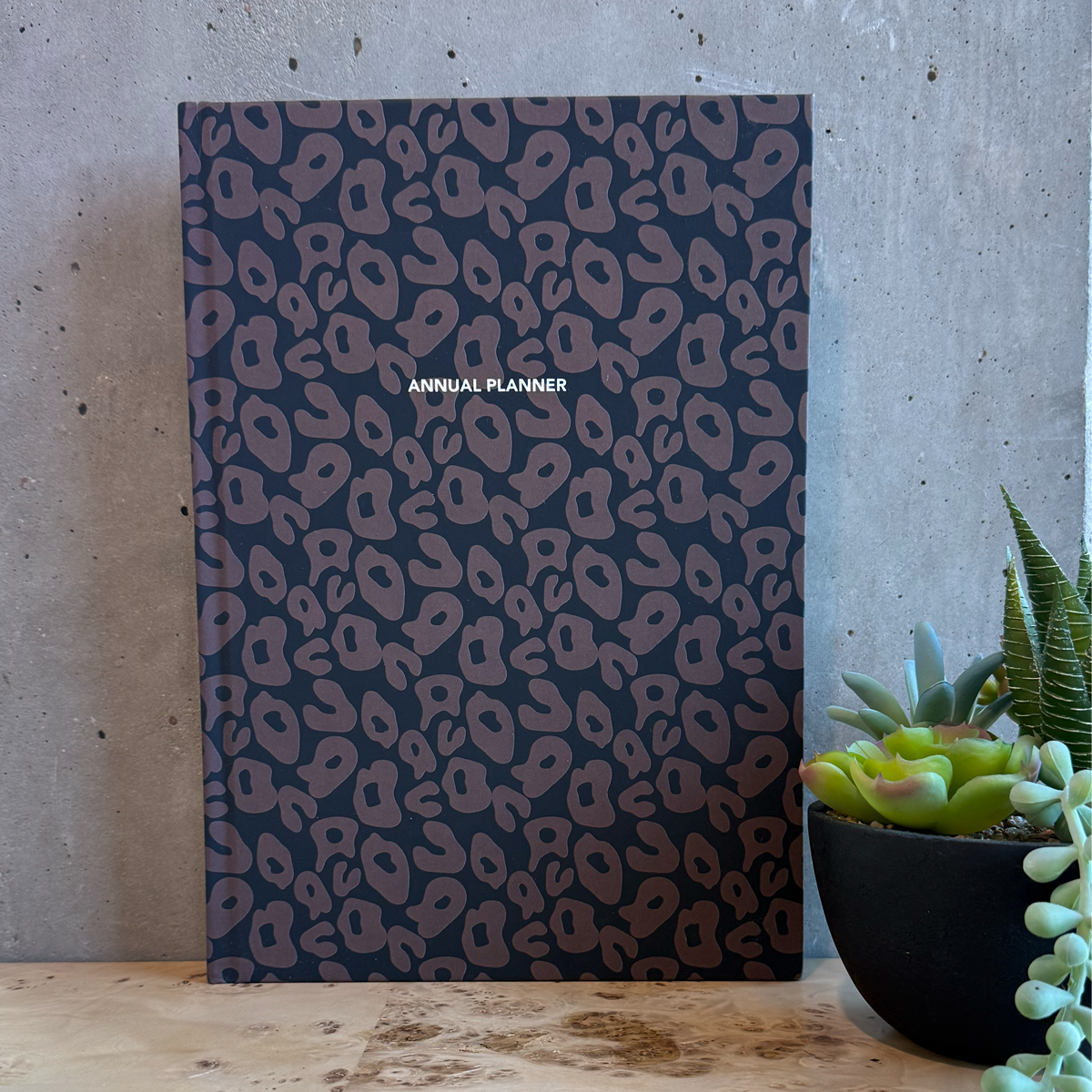 Annual planner with leopard print design on a wooden desk with a plant in the background