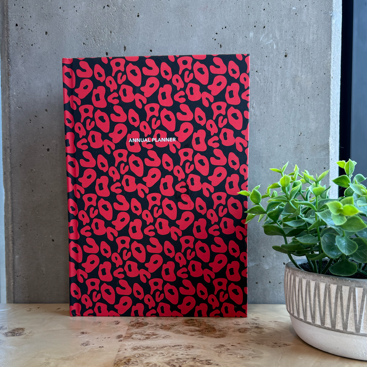 Red and black patterned annual planner on a wooden desk with a plant in the background